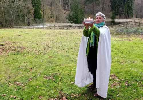 &Auml;ona, Priesterin der G&ouml;ttin Holle, h&auml;lt eine brennende Kerze bei einem Ritual im Freien
